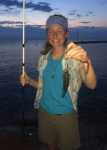 a young woman holds a fish and a fishing rod while standing on a beach