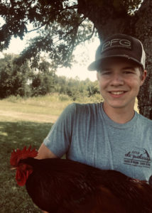 a young man standing under a tree holding a chicken